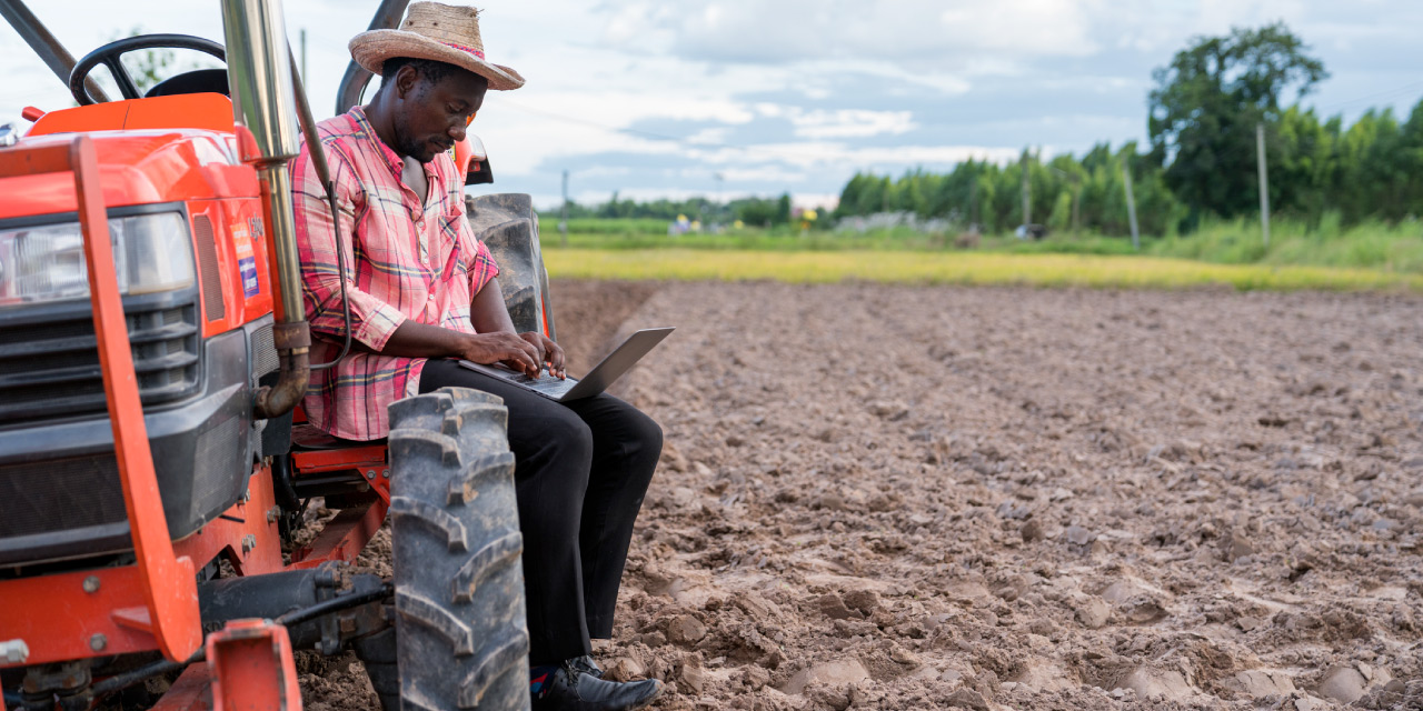 Farmer using a laptop while sitting on tractor in farm field