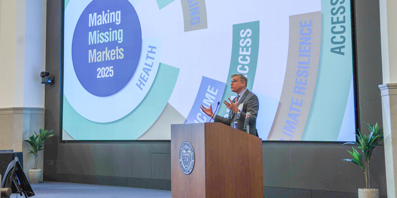 speaker at podium on stage with event title on projection screen