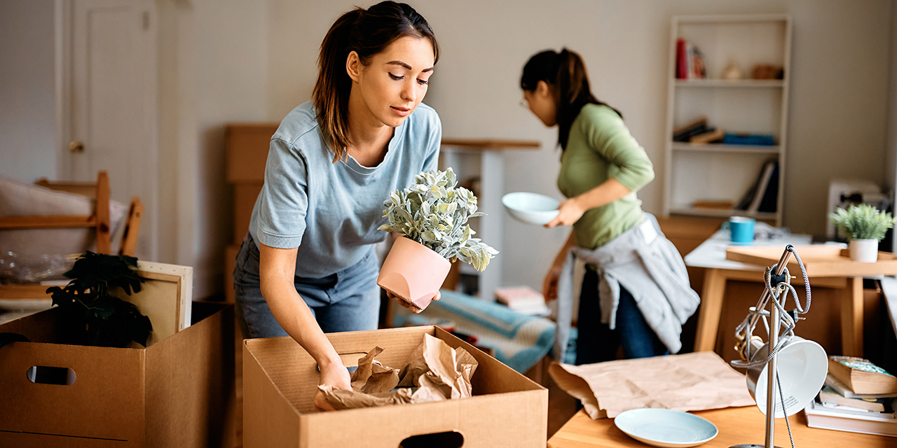 two women packing household items into cardboard moving boxes two women packing household items into cardboard moving boxes