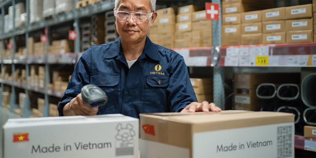 Worker wearing safety glasses and a blue uniform in a warehouse setting with shelves and packages