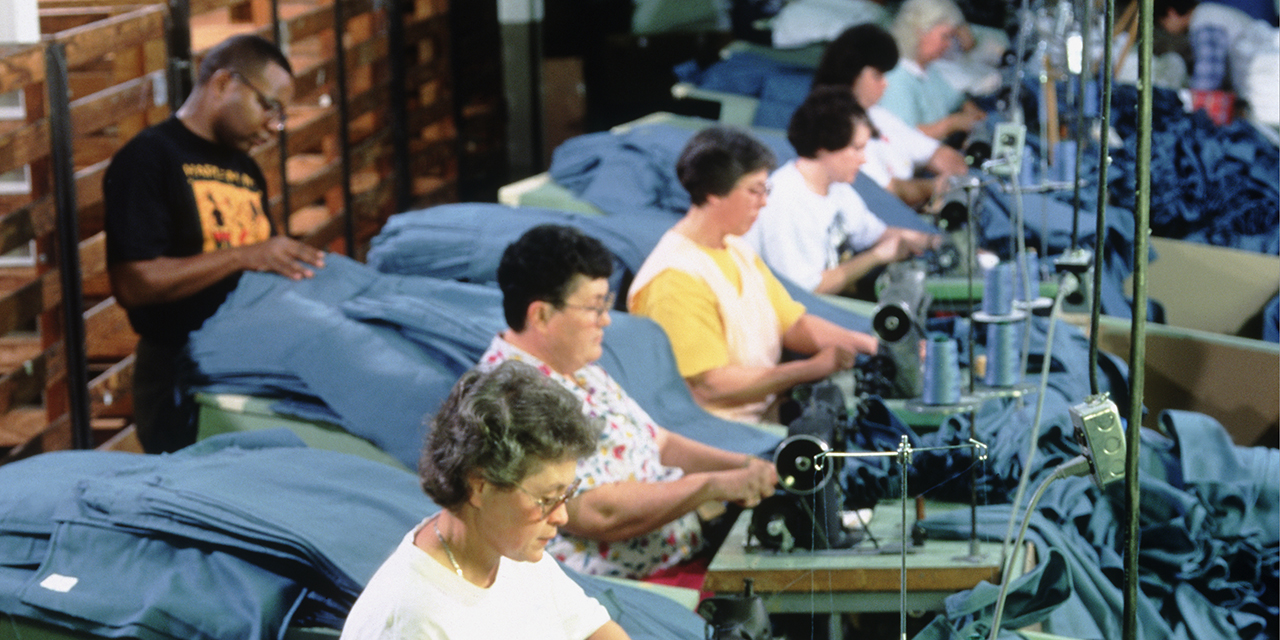Photo of men and women sitting at sewing machines all in a row handling blue material