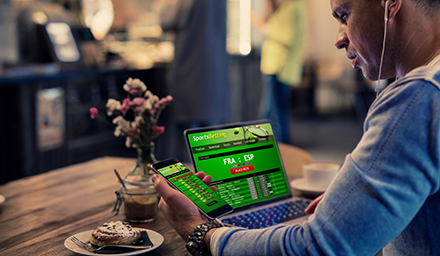 Photo: Man using online sports betting services on phone and laptop