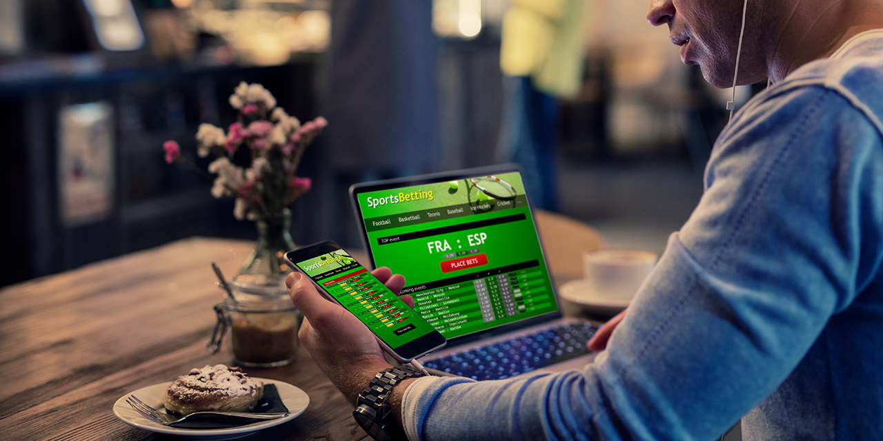Man using online sports betting services on phone and laptop