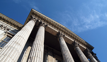 Looking up at a classical stone building with columns with blue sky in the background