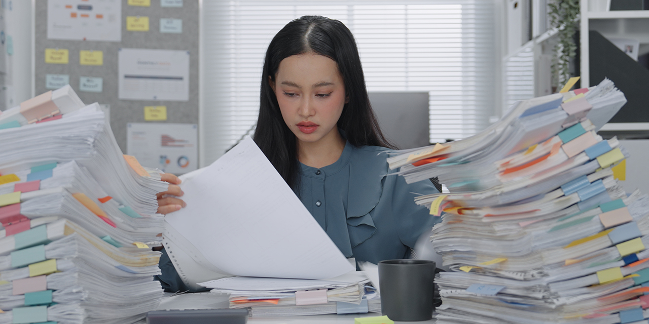 person reading a document while seated at desk piled high with paperwork person reading a document while seated at desk piled high with paperwork