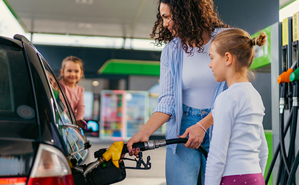 the mother fills the car with fuel at the gas station and talks to her daughters about the upcoming trip