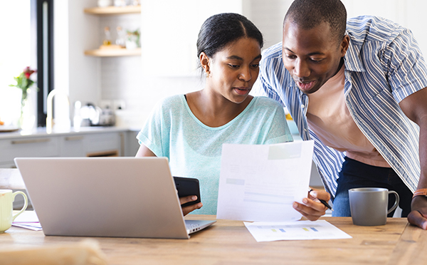 Woman sitting at kitchen table with a bill in hand and a man looking over shoulder with laptop open in front of them